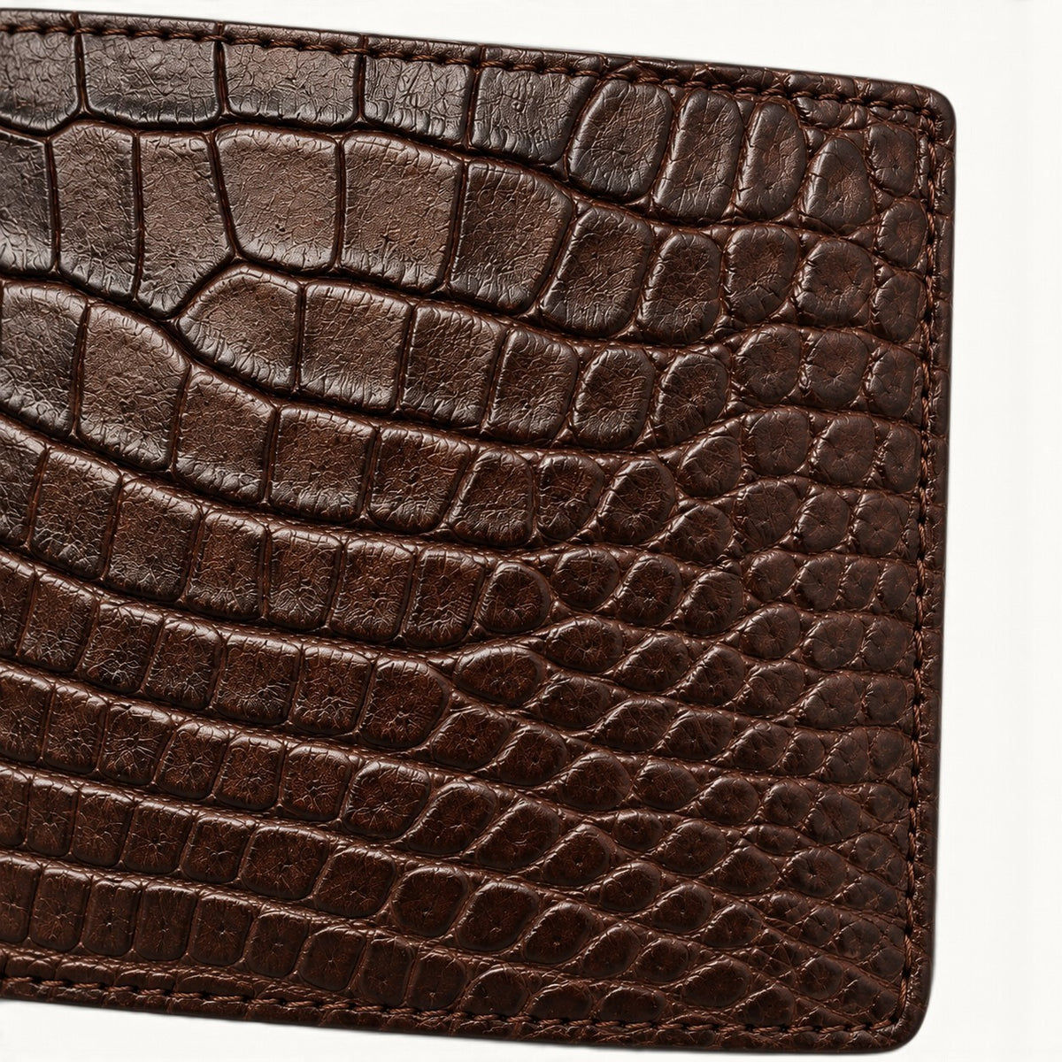 Close-up of genuine brown Siamese crocodile leather on The Ashford bifold wallet, highlighting natural scales, fine grain, stitching, and handcrafted edge detail.
