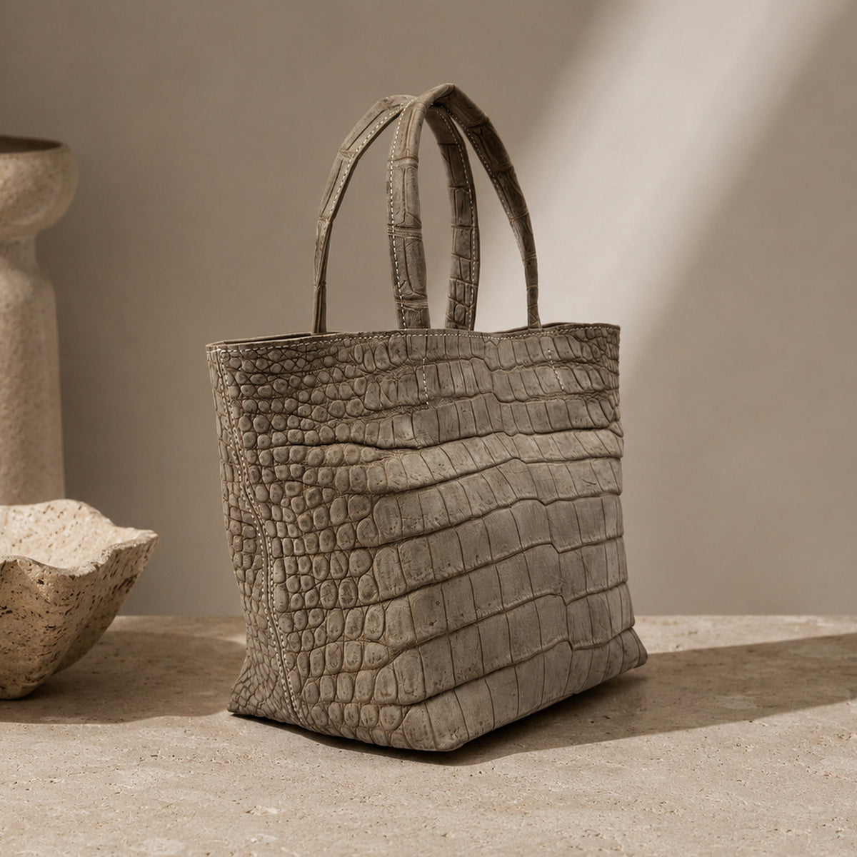 The Atelier Tote handcrafted from genuine Porosus crocodile leather, displayed in a refined interior setting that highlights the natural scale pattern and artisanal craftsmanship.