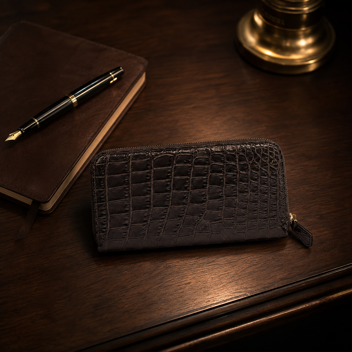 Belvedere Nicotine Brown Siamese crocodile zip-around wallet styled on a dark wood desk with leather notebook, fountain pen, and brass accents