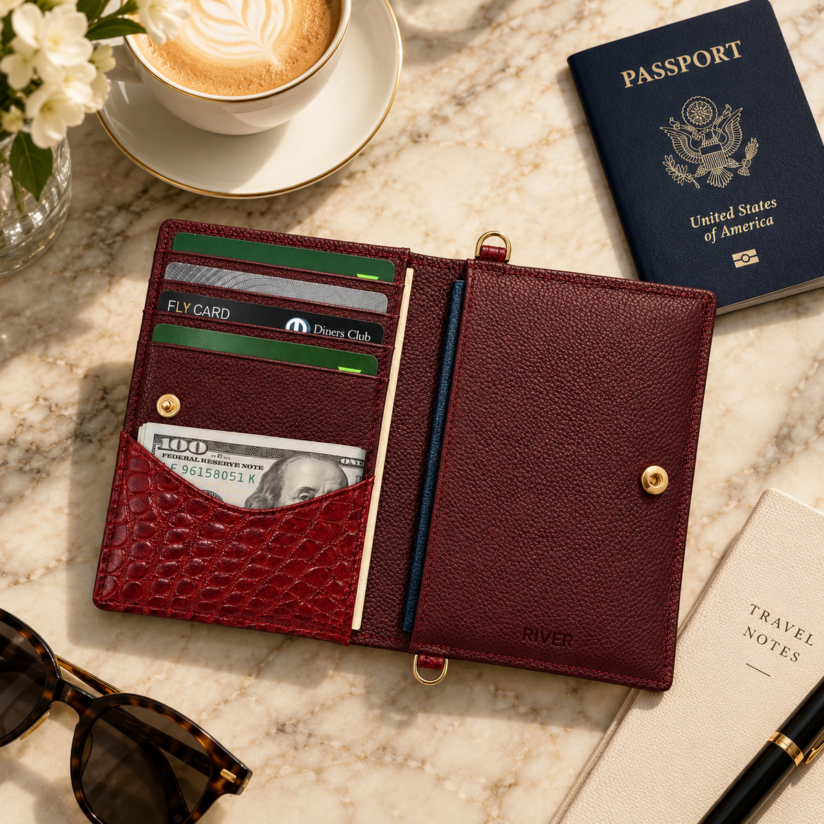 Open Berkeley Crocodile Convertible Wallet in Burgundy with cards and cash beside a U.S. passport in a luxury travel setting.