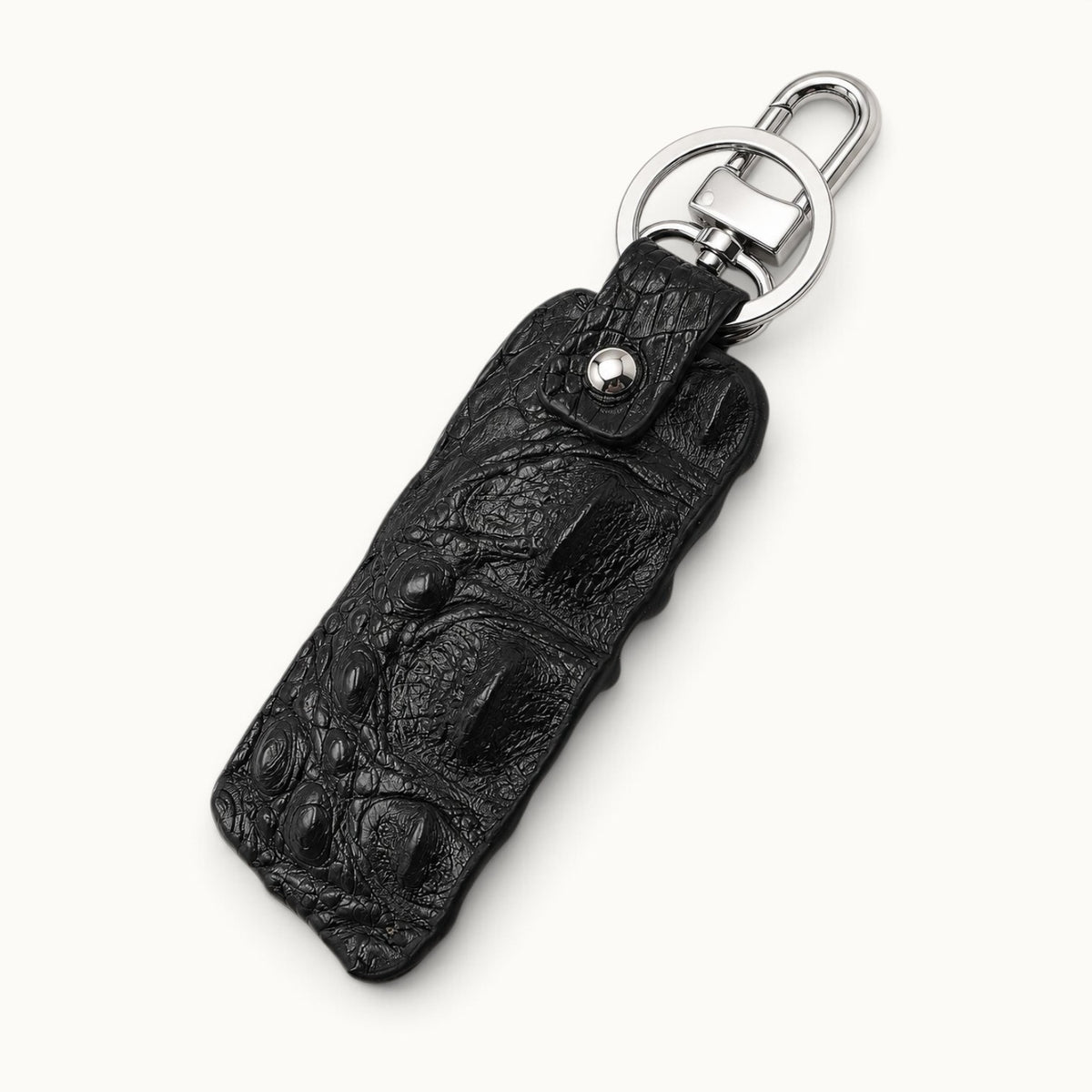 Black crocodile leather key fob in angled view with polished silver-tone clasp and large key ring on a light neutral background.