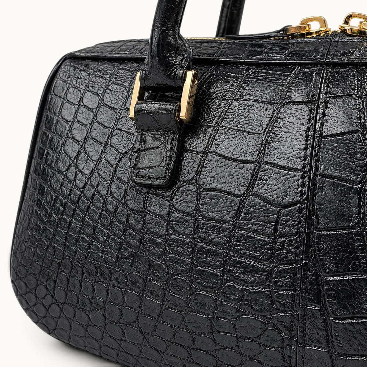 Close-up detail of the black crocodile leather top handle bag showing the scale texture, gold hardware, and handle attachment.
