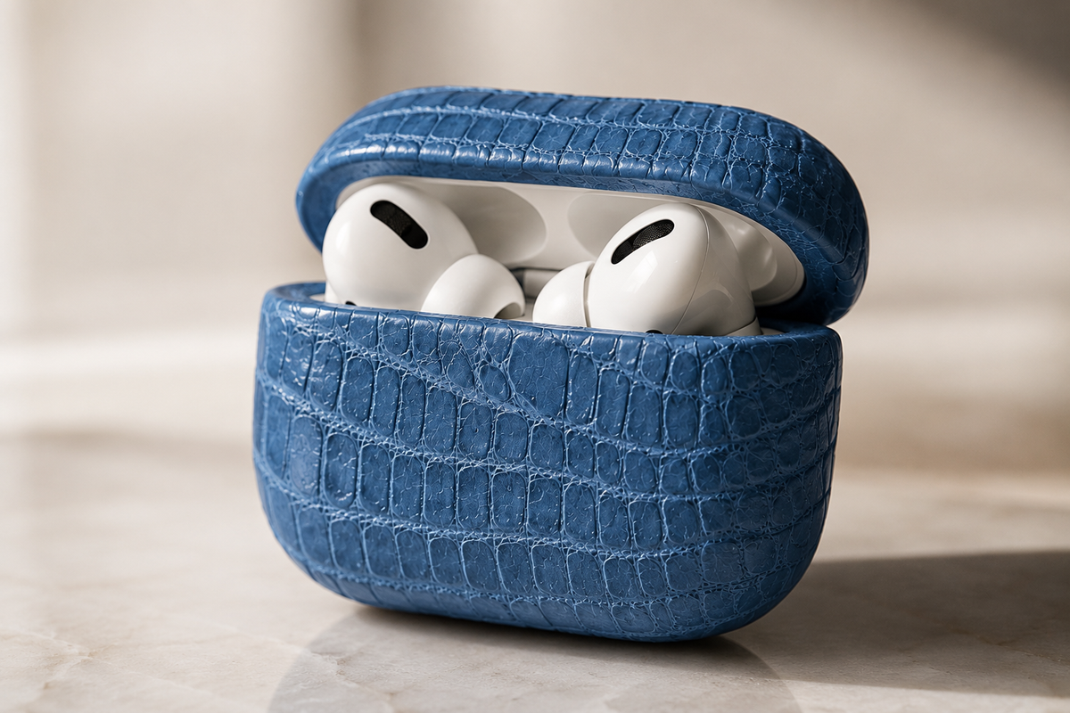 Close-up of a blue genuine crocodile leather AirPods case open with white AirPods visible, highlighting the natural scale pattern and protective fit.
