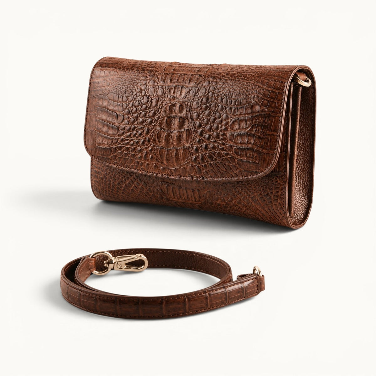 The Cavendish genuine caiman crocodile leather clutch bag in rich brown displayed with its detachable shoulder strap and polished metal clips.