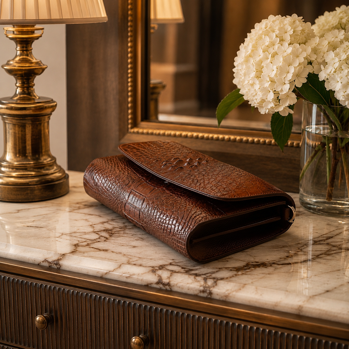 The Cavendish genuine caiman crocodile leather shoulder clutch in rich brown displayed on a marble console in an elegant interior, highlighting its natural scale pattern, rounded structure, and luxury craftsmanship.