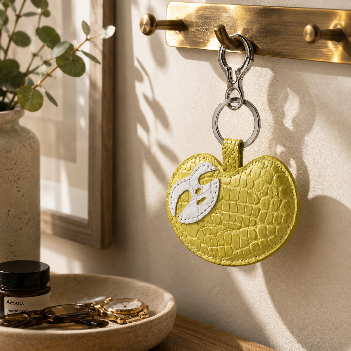 Mustard Yellow Crocodile Palette Bag Charm hanging from a brass wall hook in a refined home entryway