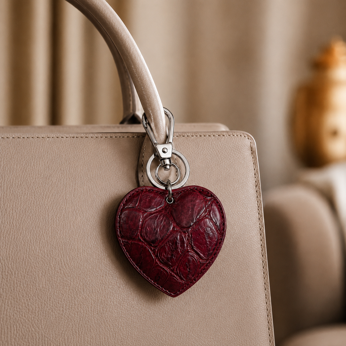 Deep Burgundy crocodile heart key charm attached to a beige leather bag handle, luxury lifestyle close-up in genuine Siamese crocodile leather.