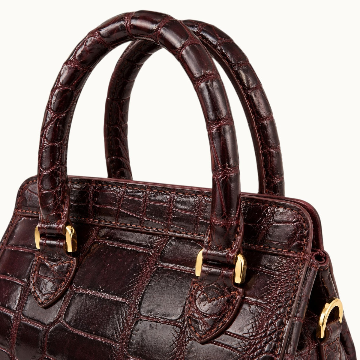 Detailed view of The Ellery Crocodile Handbag's rolled Bordeaux crocodile leather handles, stitching, and polished gold-tone attachments.