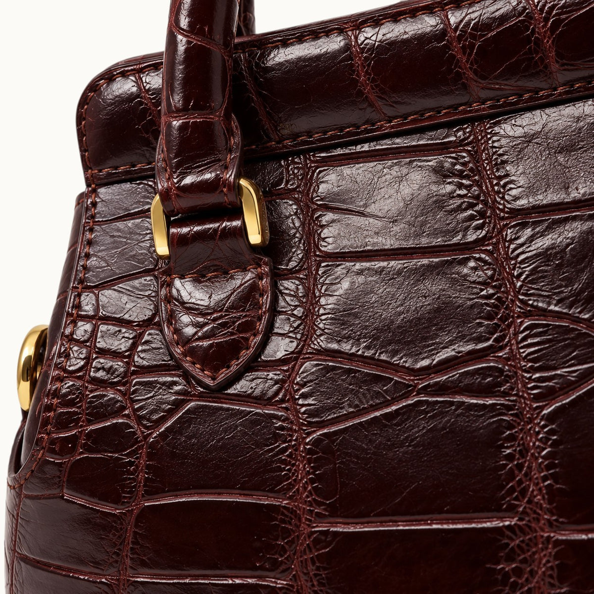 Close-up of genuine Bordeaux Siamese crocodile leather showing natural scale patterns, fine stitching, and gold-tone handle hardware.