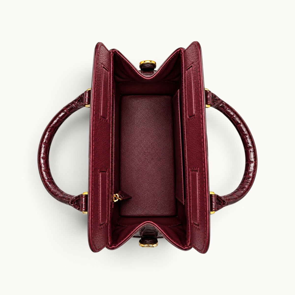 Overhead view of The Ellery Crocodile Handbag in Bordeaux, showing its open main compartment, full-grain cow leather lining, interior pockets, and magnetic closures.
