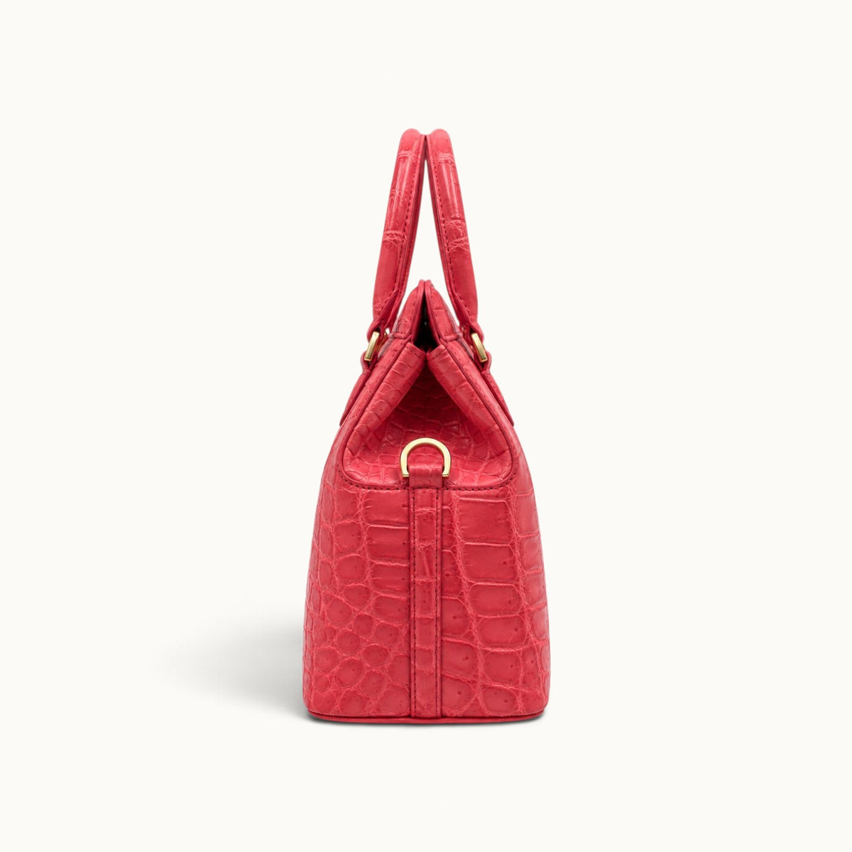 Side view of The Ellery Crocodile Handbag in Coral Pink, showing its structured gusset, rolled handles, and gold-tone shoulder strap D-ring.