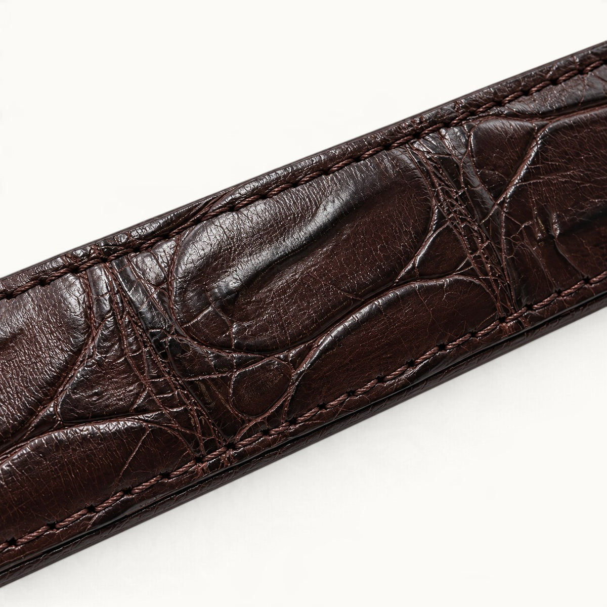 Detailed view of rich dark brown crocodile leather with distinctive natural scale patterns and precision edge stitching.