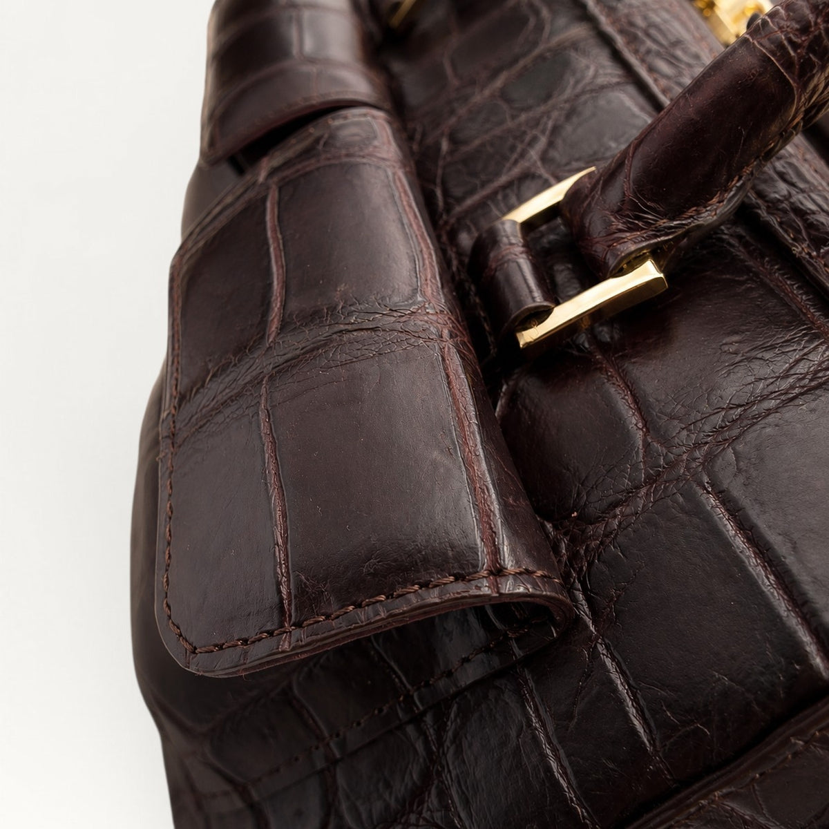 Close-up detail of espresso brown crocodile leather texture, stitching and polished gold-tone handle hardware