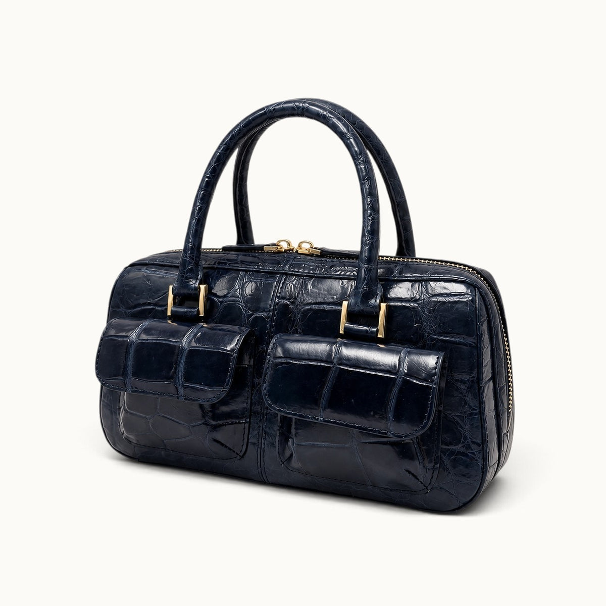 The Fairmont Crocodile Handbag in navy blue shown in an angled view with structured silhouette, gold-tone hardware, and front pockets.