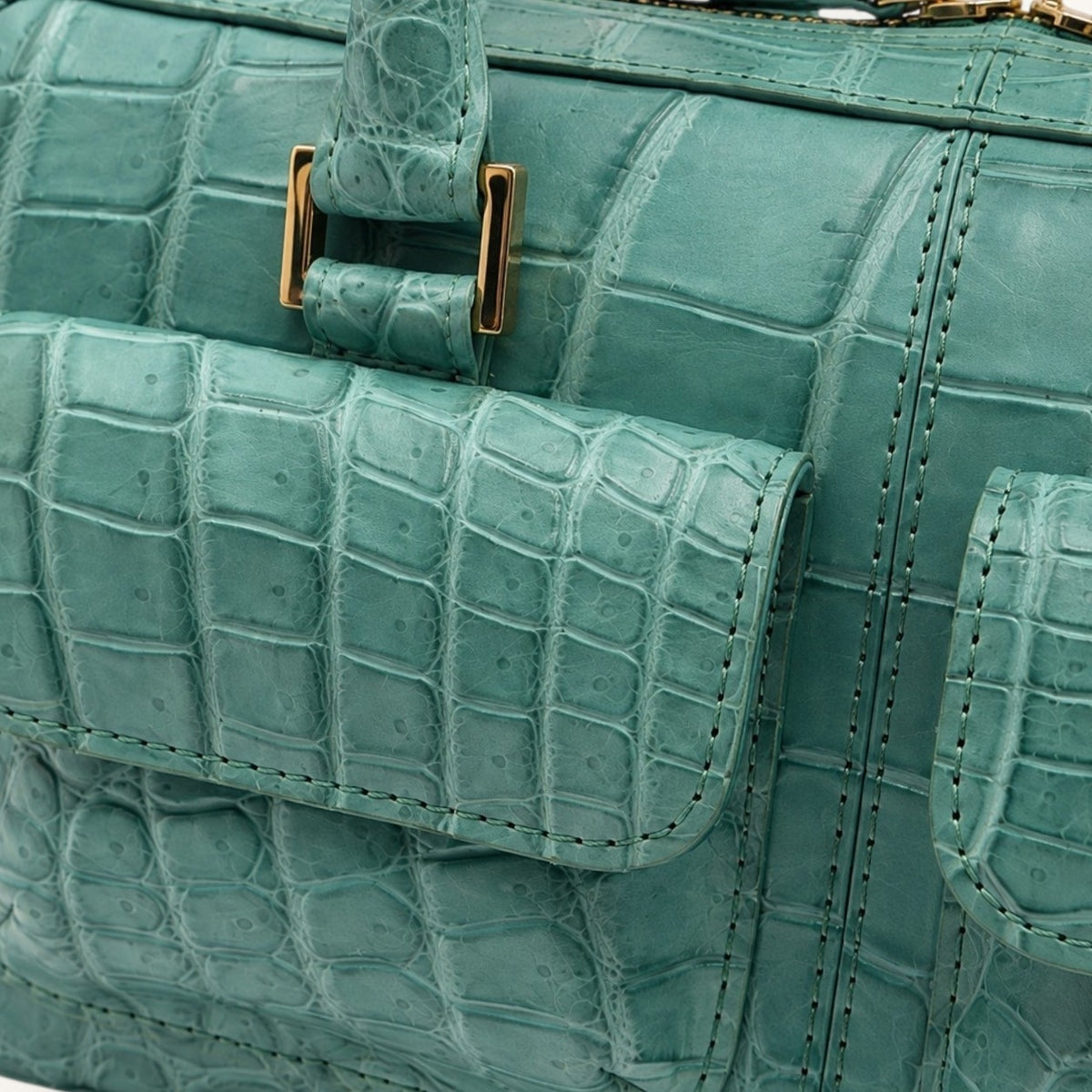 Close-up detail of the Fairmont Seafoam Green Siamese crocodile handbag showing the scale texture, stitching, front pocket, and gold-tone hardware.