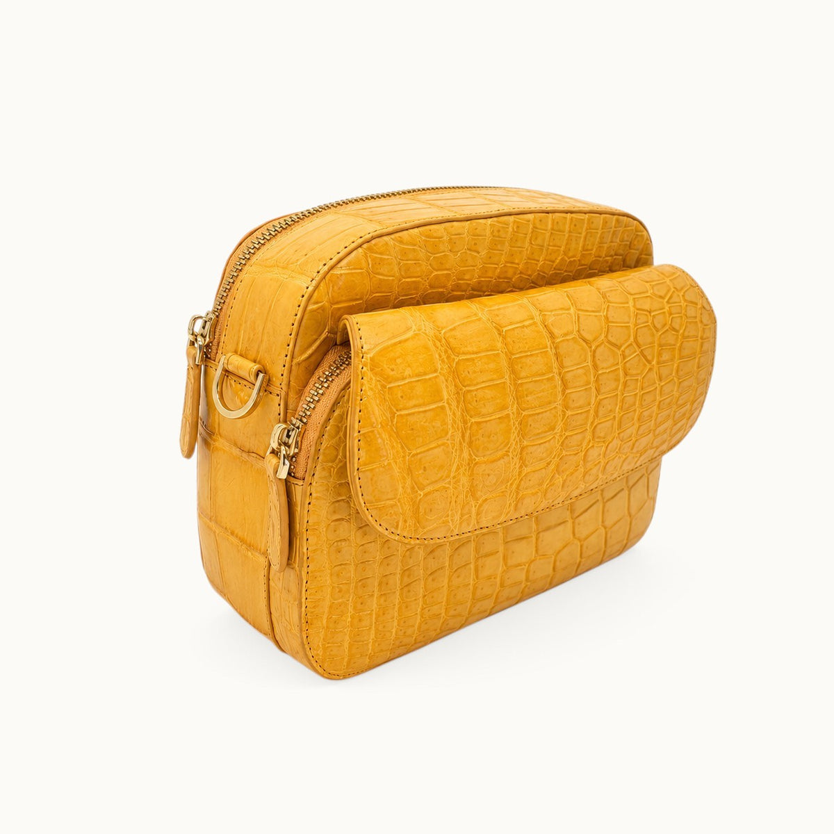 Three-quarter angle view of the Grosvenor Siamese crocodile crossbody bag in Golden Mustard, showing the front flap, zipper compartments, and side D-ring.