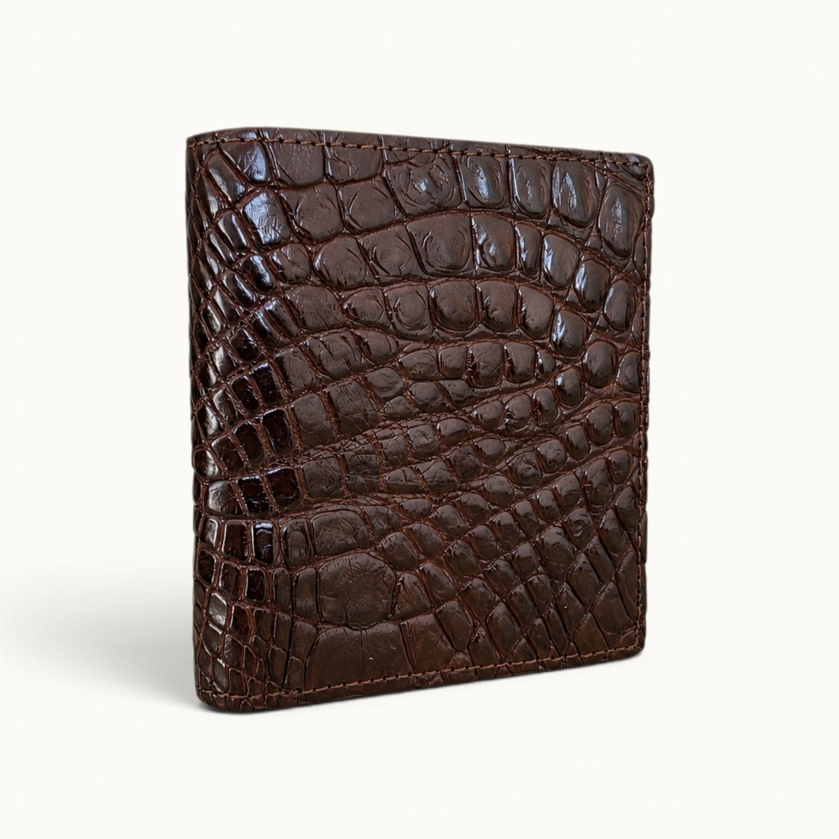 Herrington Espresso Brown genuine Siamese crocodile trifold wallet shown from an angled view, highlighting its glossy natural scales, refined stitching, and slim profile.