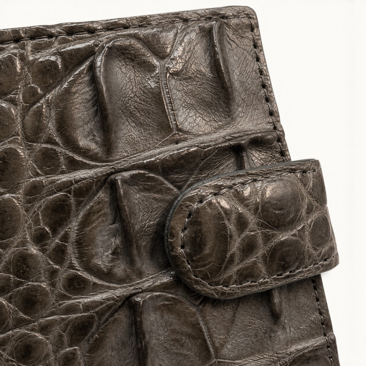 Close-up of the taupe green Langham crocodile wallet snap closure and natural scale texture