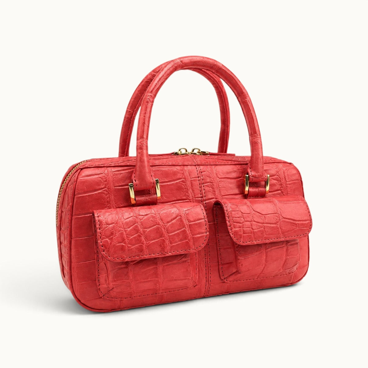 Coral red luxury crocodile top handle handbag shown at an angle with structured shape and two front pockets.