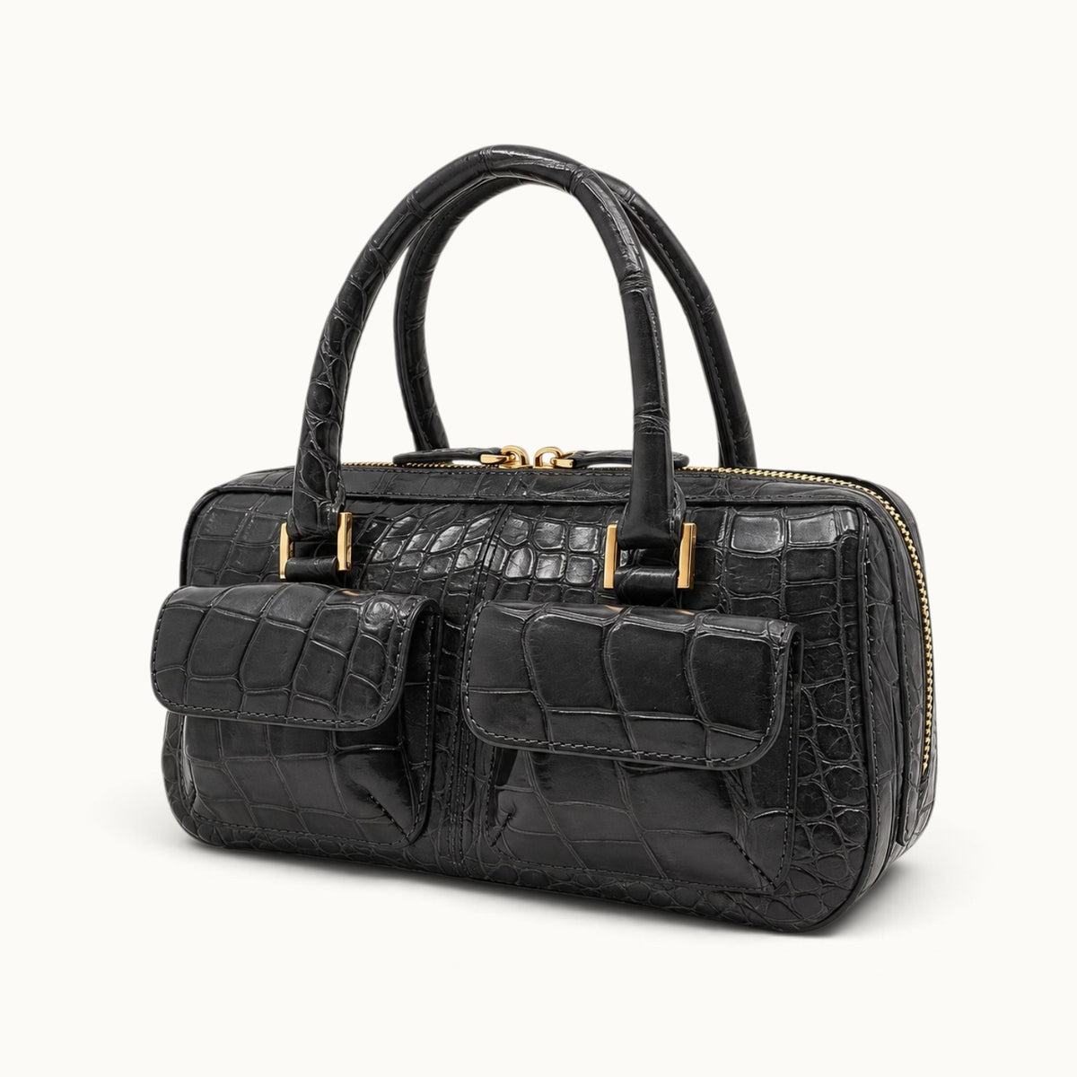 The Fairmont Crocodile Handbag in gunmetal shown at a three-quarter angle with dual flap pockets, structured top handles, gold-tone hardware, and zip-top closure.