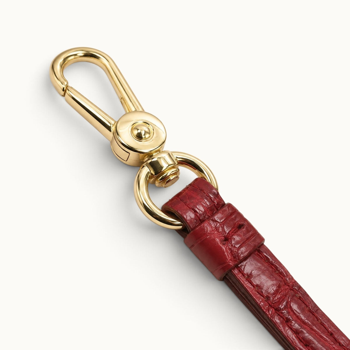 Close-up of the Burgundy Red Stanhope crocodile wrist strap with polished gold-tone swivel clasp, ring hardware, stitching, and leather keeper.