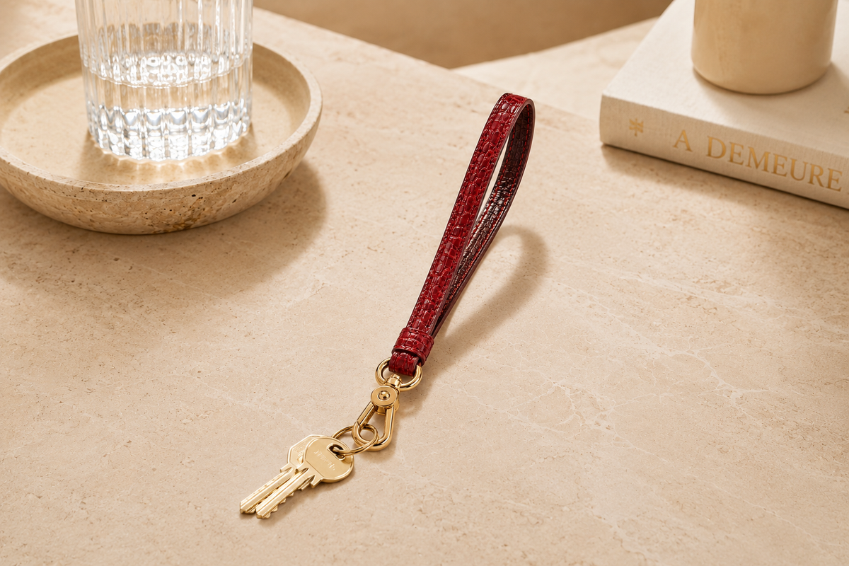 Burgundy Red Stanhope crocodile wrist strap with gold-tone clasp and keys on a warm cream stone surface.