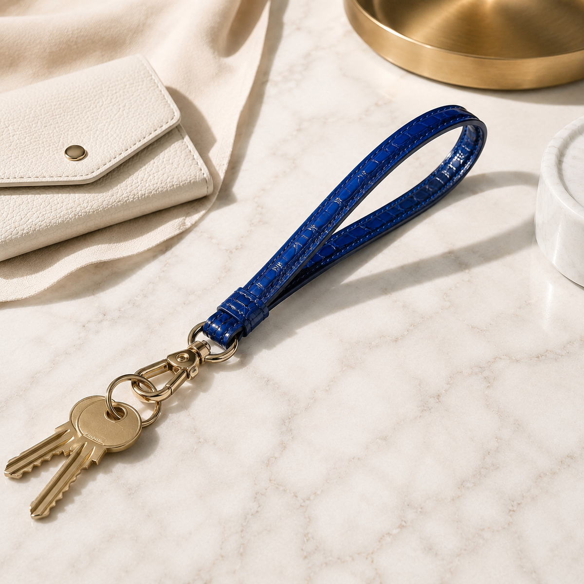 Royal Blue Stanhope crocodile wrist strap with gold-tone clasp and keys on a cream marble surface.