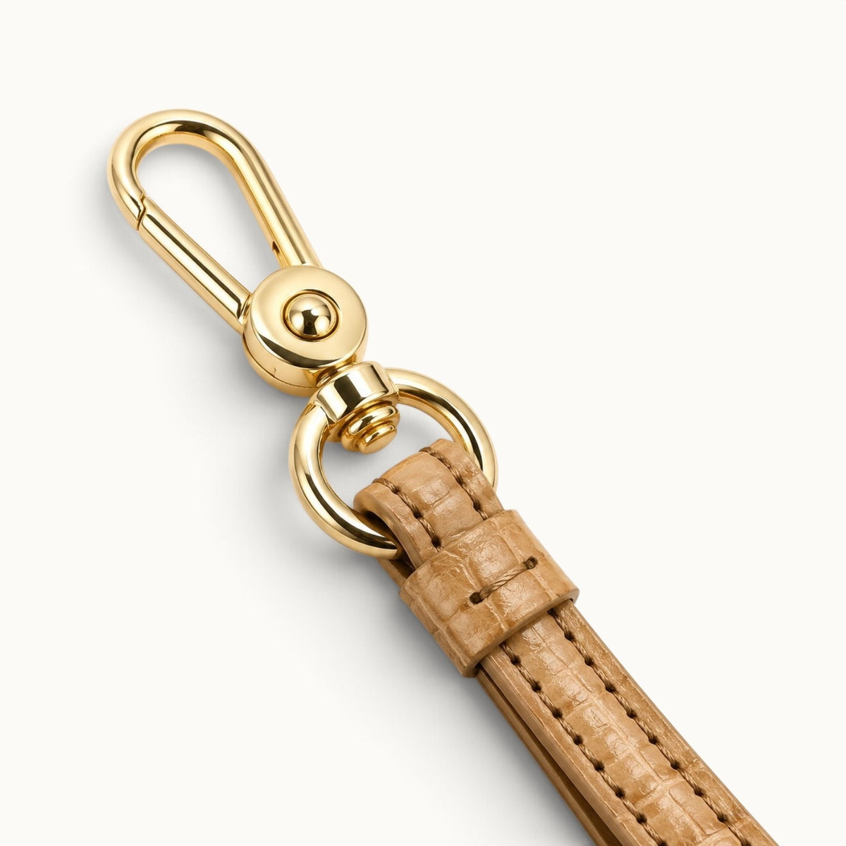 Close-up of the Sand Beige Stanhope crocodile wrist strap with polished gold-tone swivel clasp, ring hardware, stitching, and leather keeper.