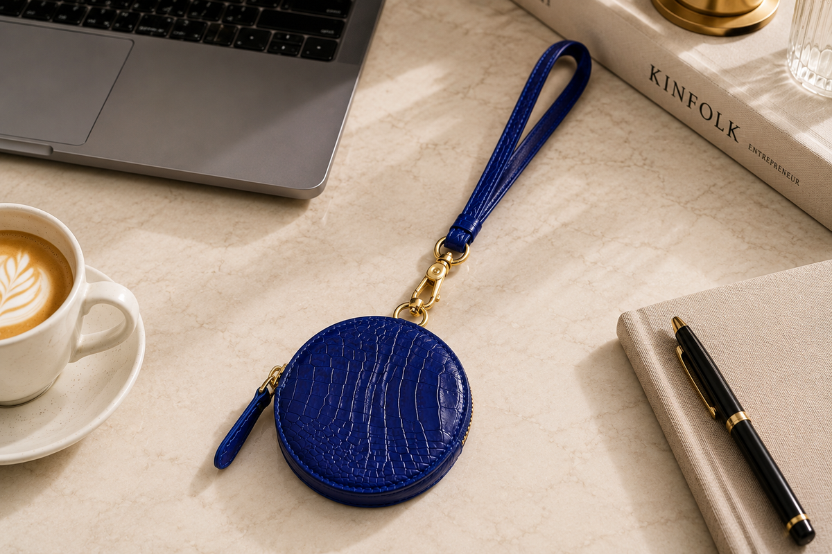 Royal Blue Stanhope crocodile wrist strap with gold-tone clasp attached to a matching round crocodile pouch on a refined desk.