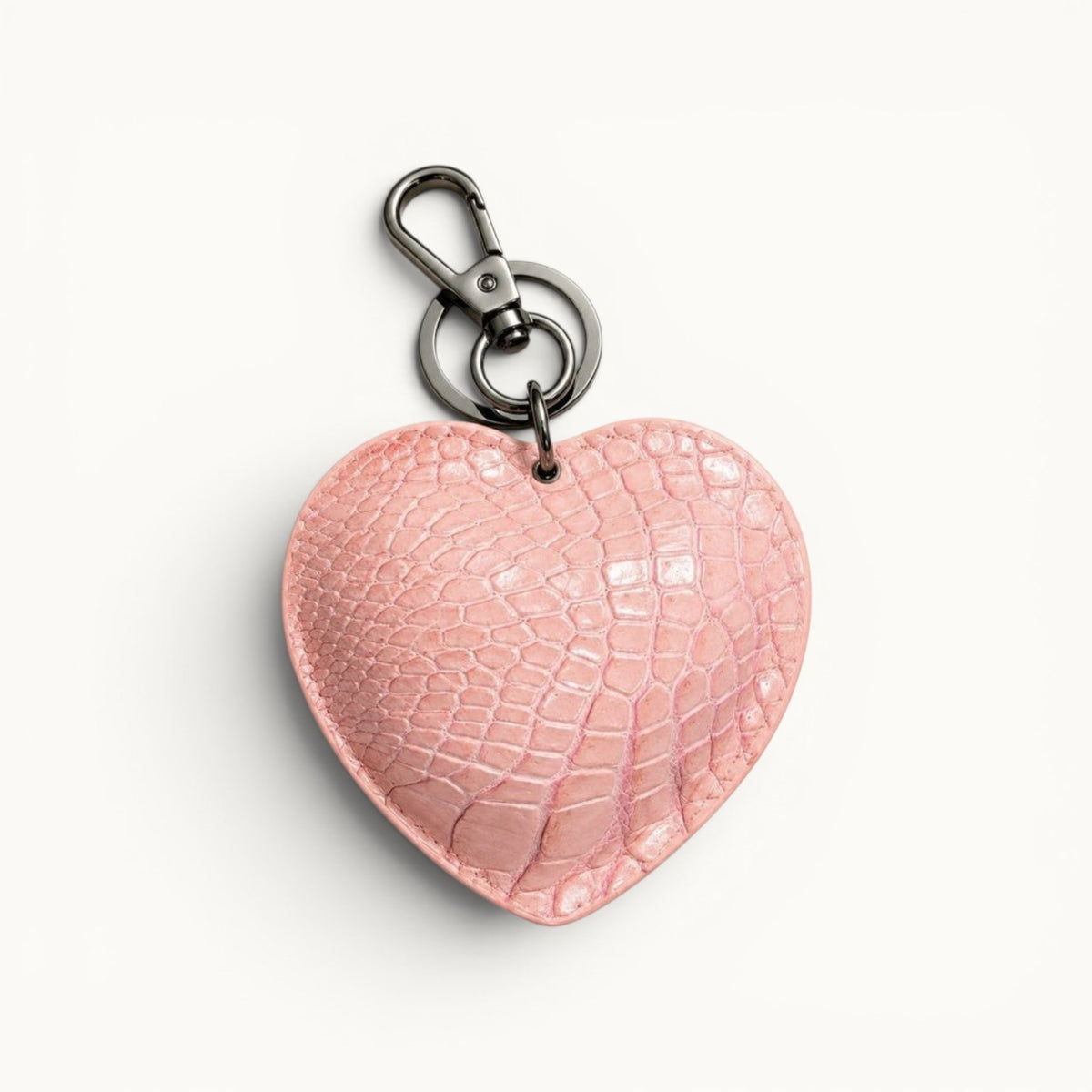 The Heart Key Charm in blush pink Siamese crocodile leather with a natural scale pattern, heart-shaped silhouette, and polished silver-tone keyring.