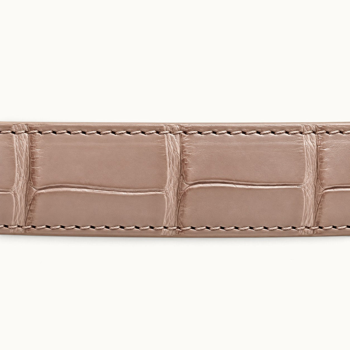 Macro photograph of genuine Siamese crocodile belly leather in Blush Pink, highlighting natural rectangular scales and detailed stitching.