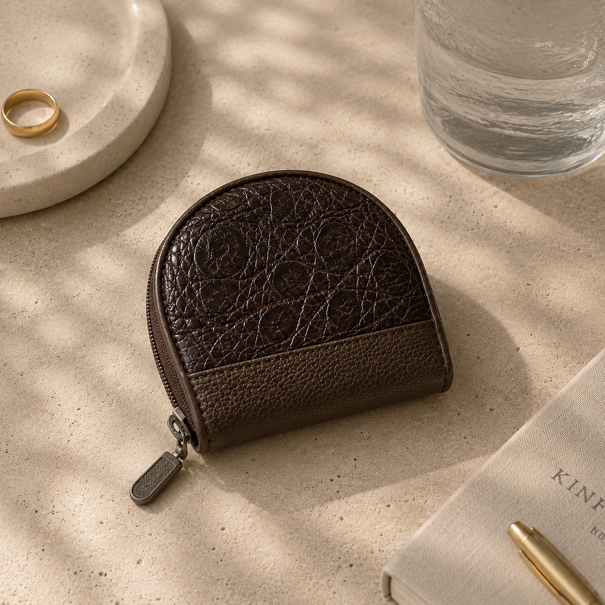 The Sovereign brown crocodile leather coin pouch styled on a stone surface with refined accessories in a luxury lifestyle setting.