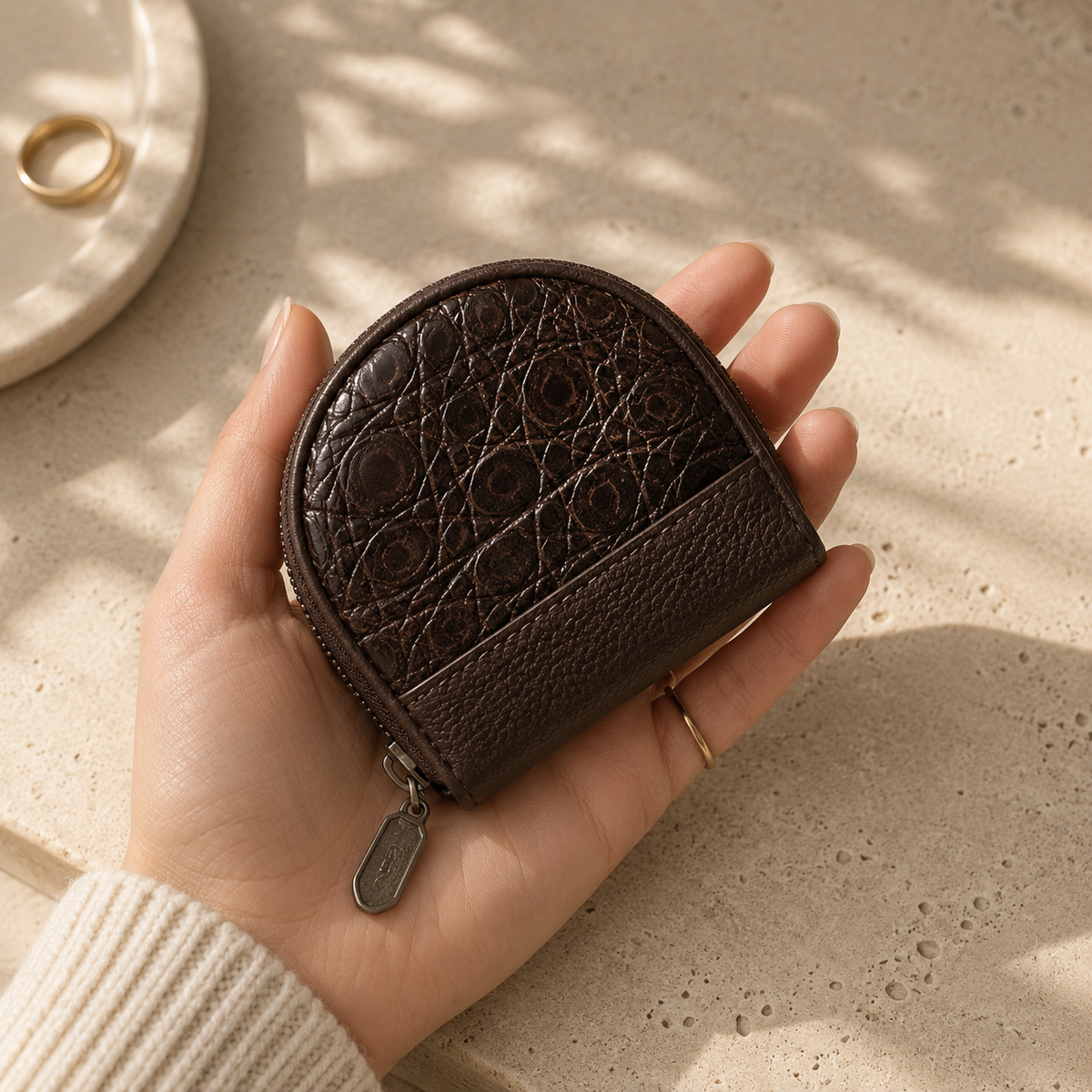 The Sovereign brown crocodile leather pocket coin purse held in hand, showing its compact size, rounded silhouette, natural scale pattern, and zip closure.