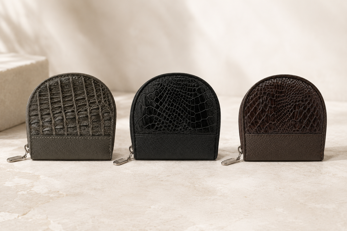The Sovereign caiman leather coin pouch collection in taupe green, classic black, and rich brown, displayed together on a refined stone surface.
