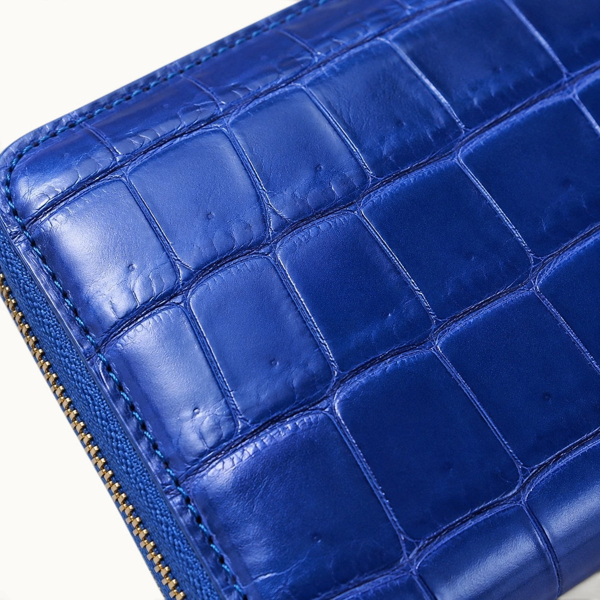 lose-up of the Belvedere Royal Blue Siamese crocodile zip-around wallet showing natural glossy scales, fine stitching, and gold-tone zipper detail.

Stone Gray