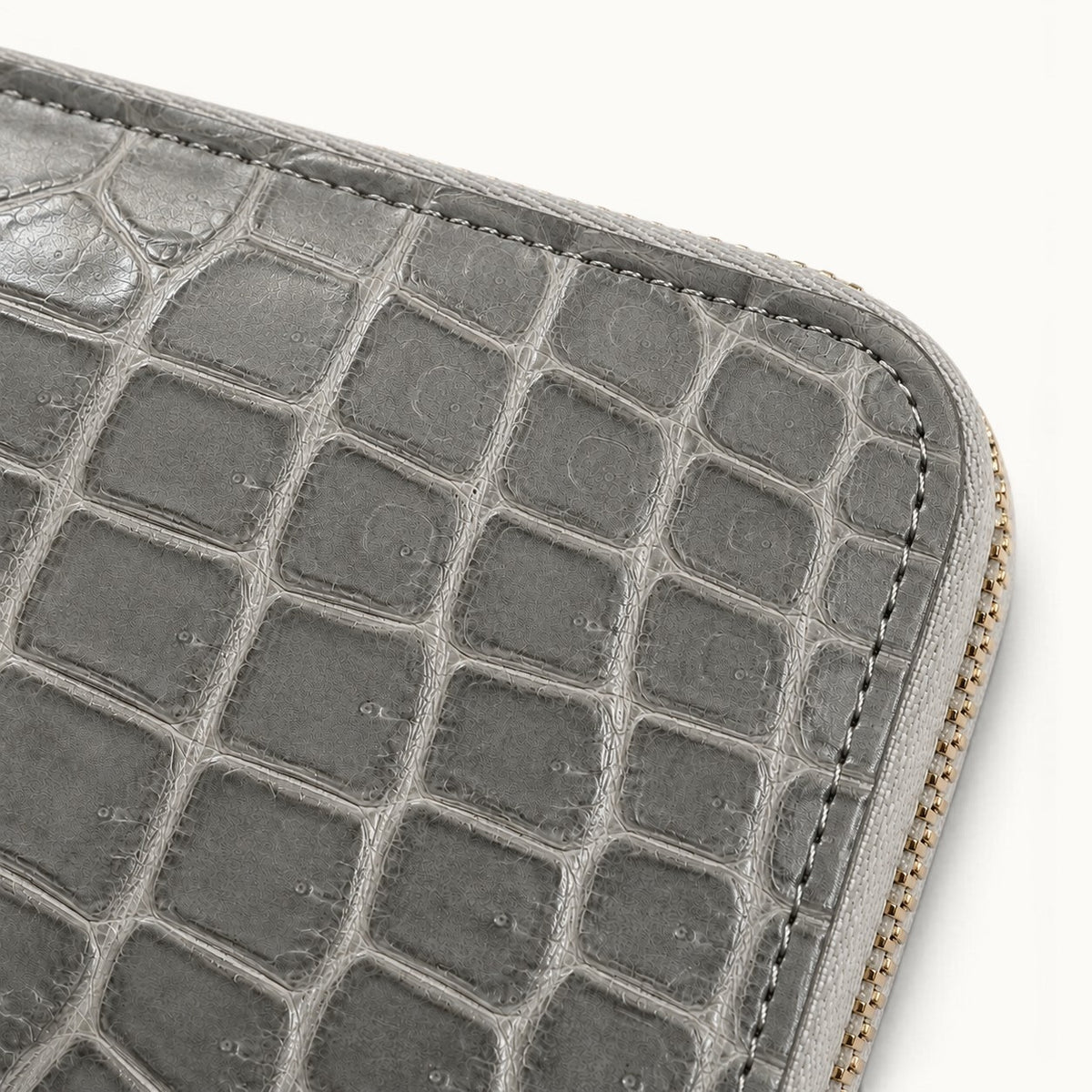 Alt text: Close-up of the Belvedere Stone Gray Siamese crocodile zip-around wallet showing natural scale texture, fine surface detail, stitching, and gold-tone zipper.