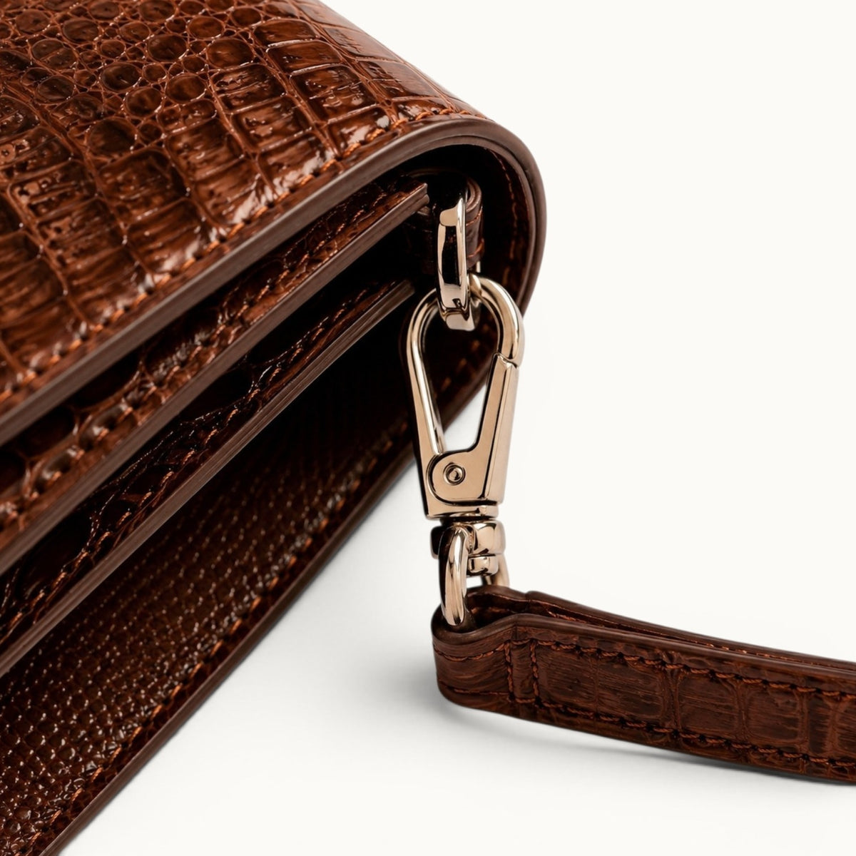 Close-up of The Cavendish genuine caiman leather shoulder clutch, highlighting the polished silver-tone strap clip, attachment ring, precise stitching, and hand-finished leather edges.