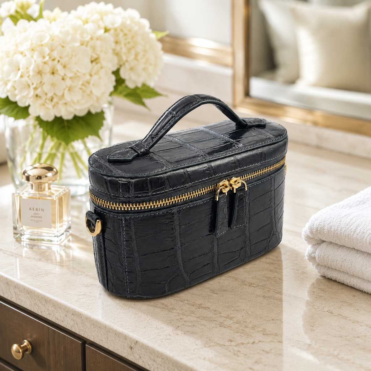 Gunmetal Gray Clarendon crocodile mini box bag styled on a luxury hotel vanity, featuring a structured Siamese crocodile leather silhouette, top handle, double gold-tone zipper pulls, and elegant travel-ready design.