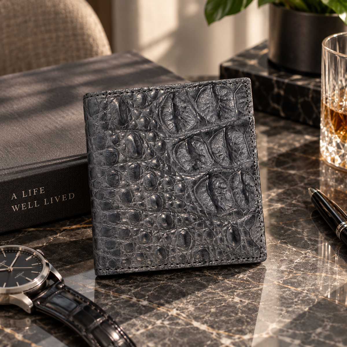 The Compact Crocodile Wallet in Graphite Gray styled in a luxury interior with watch, pen and marble details