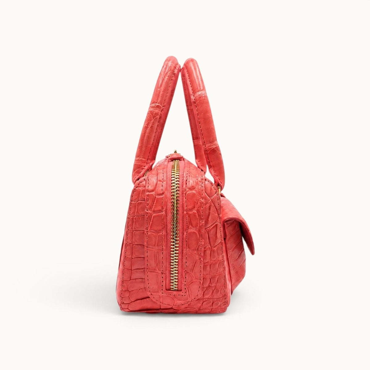 Side view of the coral red Fairmont crocodile handbag showing its structured profile and gold-tone zip closure.