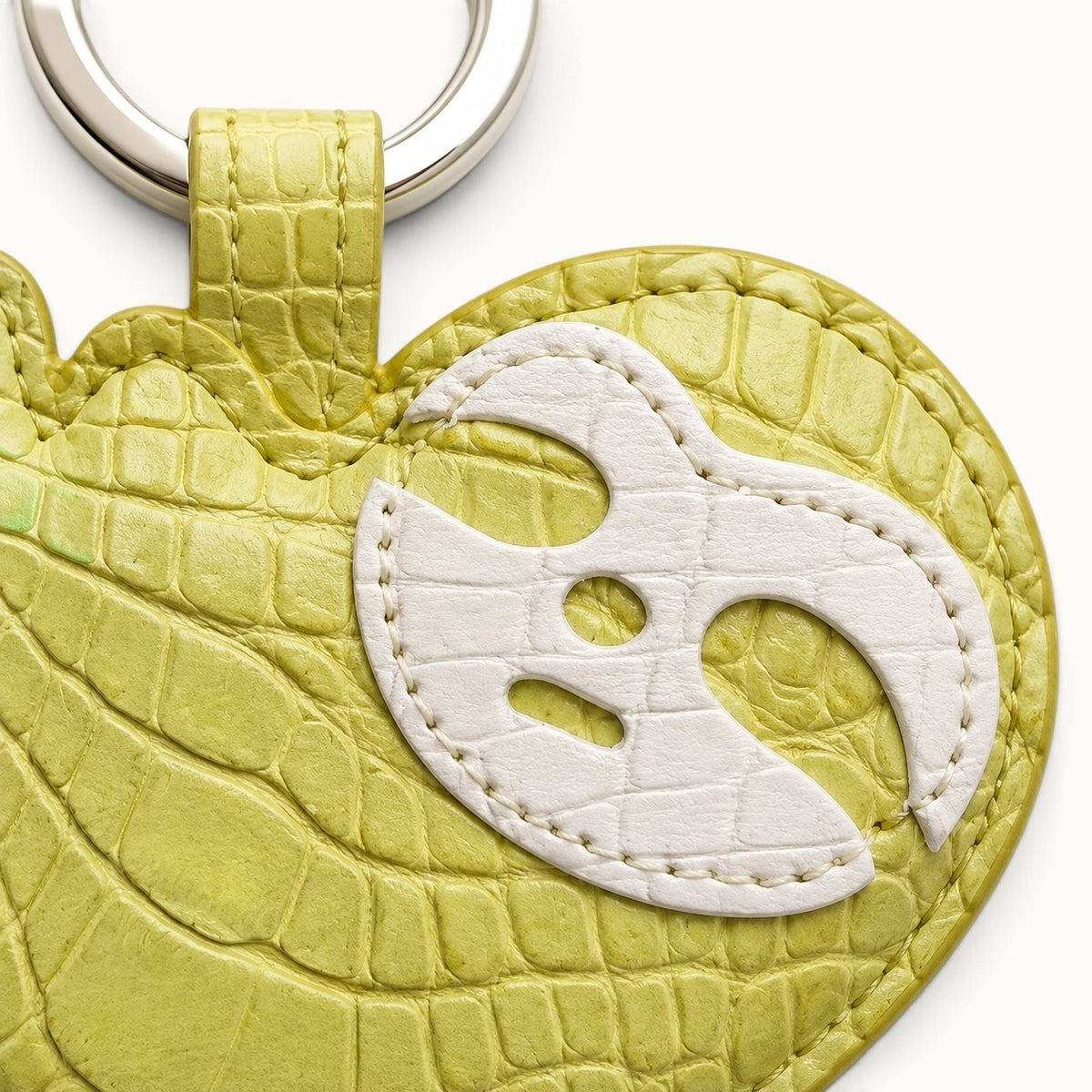 Close-up of the white leather mask motif and crocodile texture on the Mustard Yellow Crocodile Palette Bag Charm