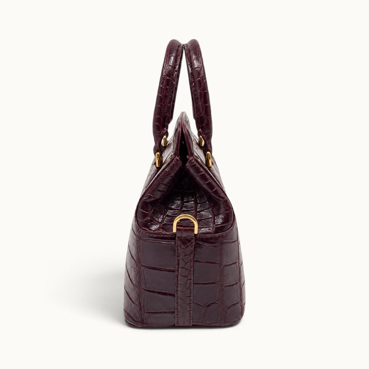 Side profile of The Ellery Crocodile Handbag in Bordeaux with triangular leather gusset, rolled handles, and gold shoulder strap D-ring.