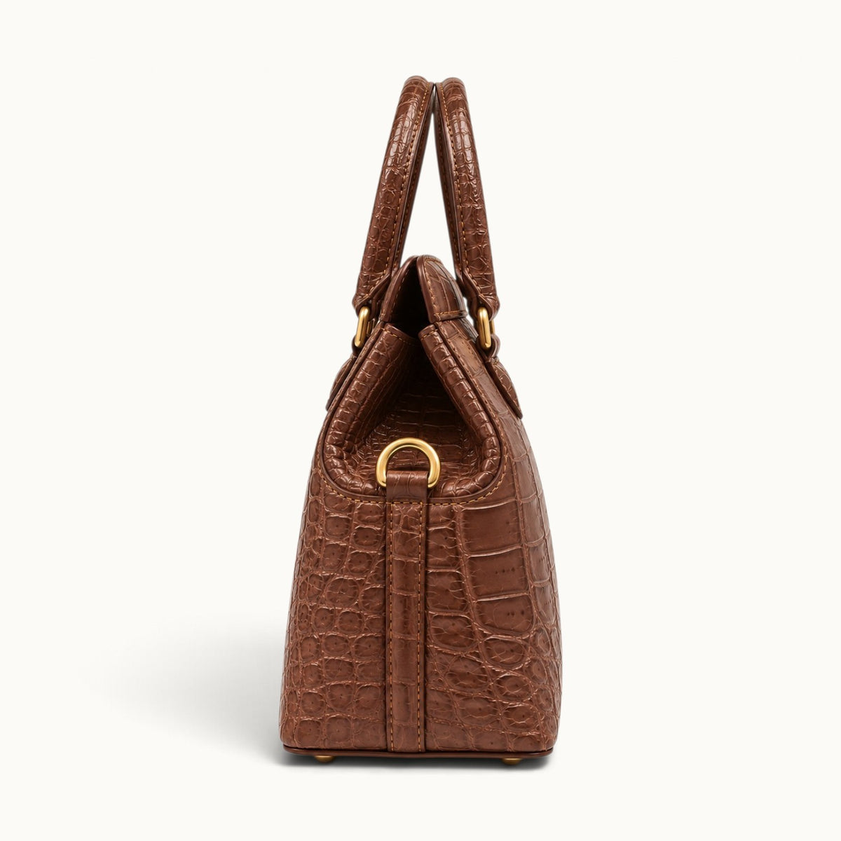 Side profile of The Ellery Crocodile Handbag in Cocoa Brown, featuring its triangular leather gusset, rolled handles, and gold-tone shoulder strap attachment.