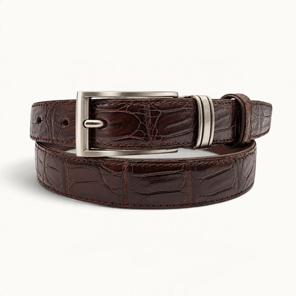The Ellington dark brown crocodile leather belt elegantly coiled with distinctive natural scales, silver-tone buckle, and matching leather keeper.