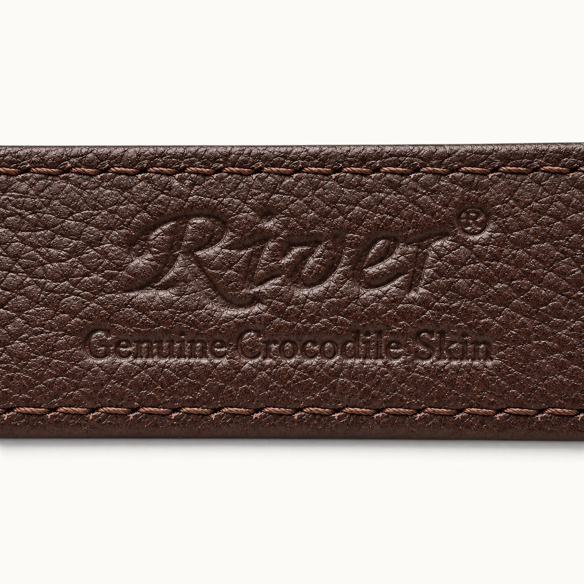 Close-up of embossed River logo and Genuine Crocodile Skin lettering on the dark brown leather lining of The Ellington belt.