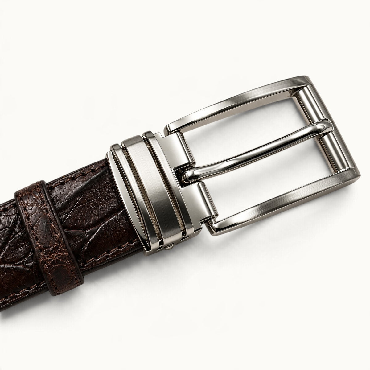 Close-up of The Ellington crocodile belt's polished silver-tone rectangular buckle, brushed metal accents, and dark brown crocodile leather.