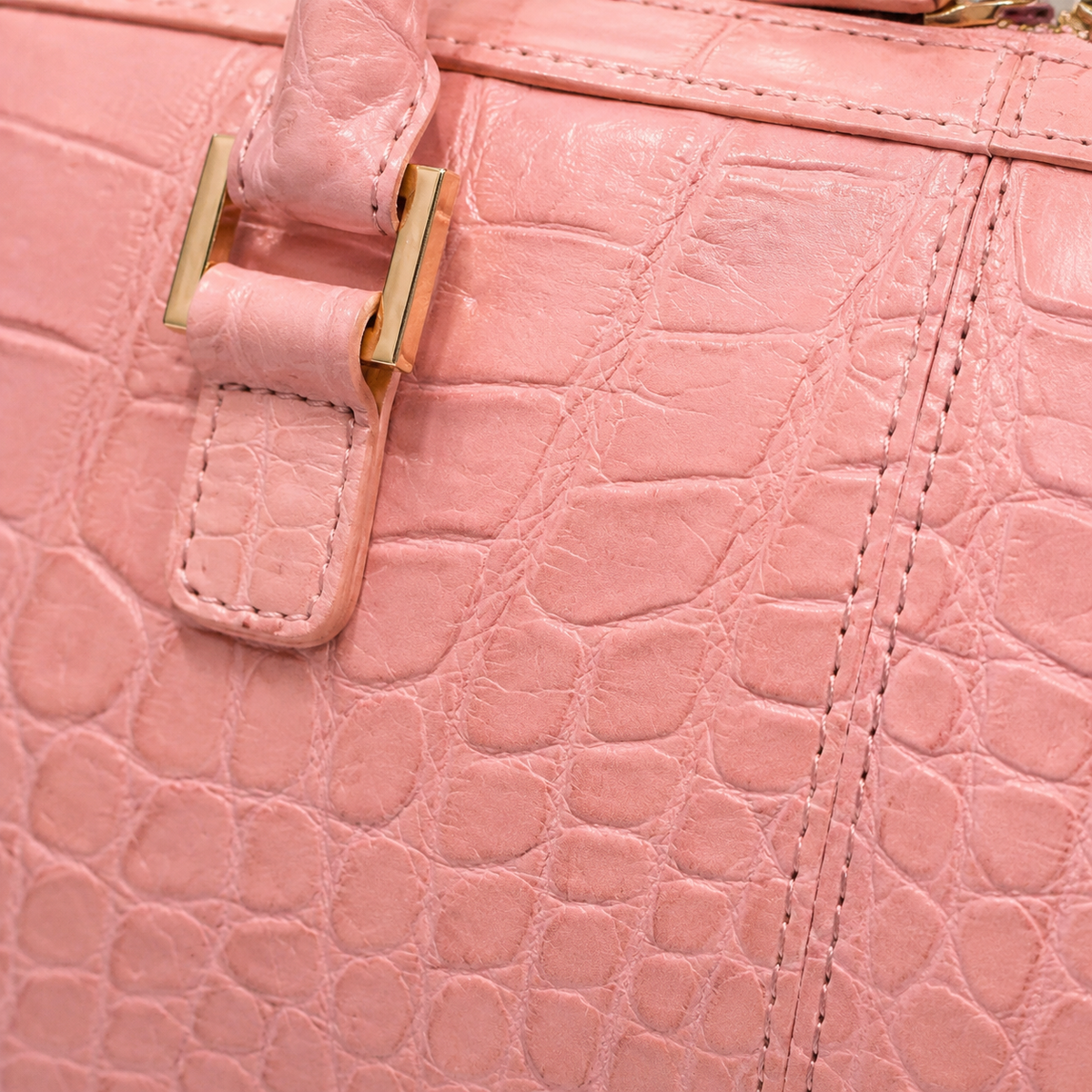 Close-up detail of The Fairmont Crocodile Handbag in blush pink showing genuine crocodile leather texture, stitching, and gold-tone handle hardware.