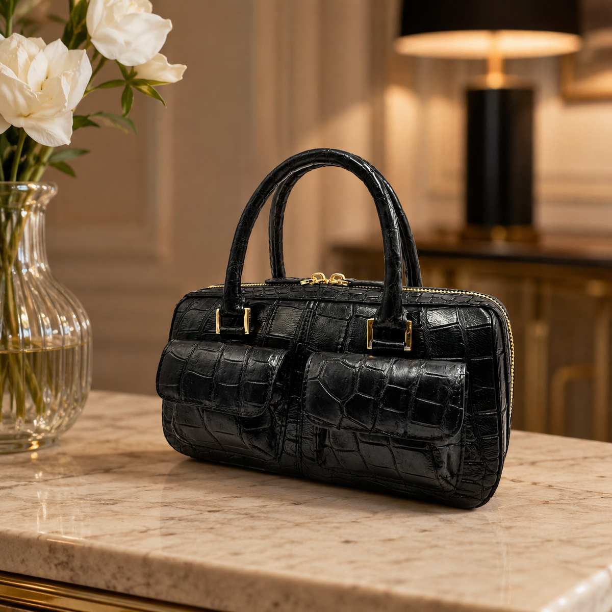 Fairmont Siamese crocodile handbag in Classic Black styled on a luxury marble console with white flowers and warm ambient lighting.