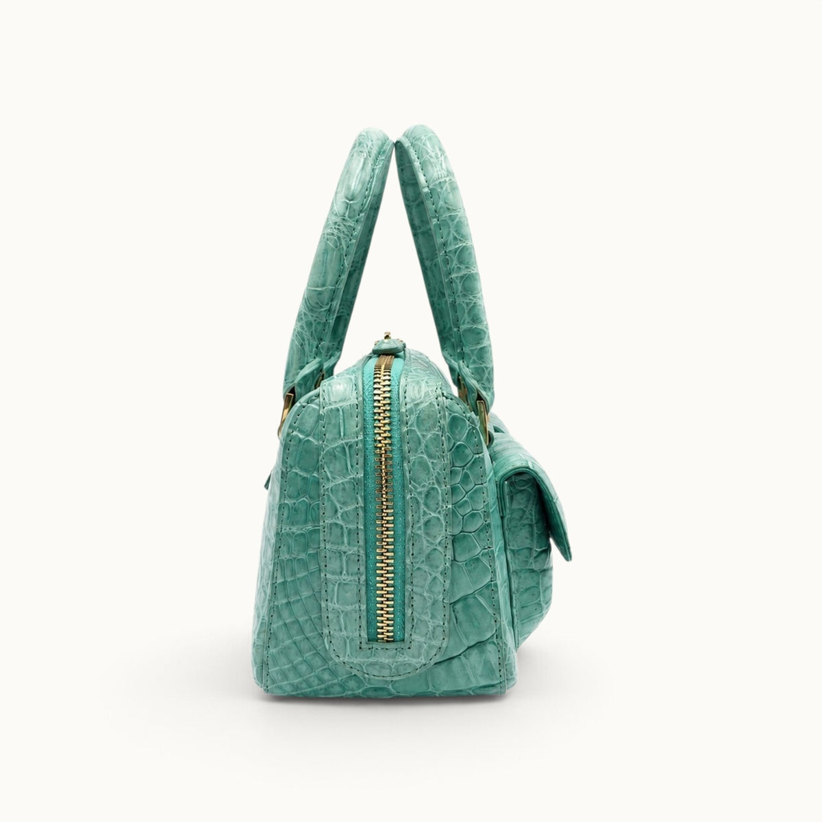 Side view of the Fairmont Seafoam Green Siamese crocodile handbag showing its structured profile, top zipper, handles, and exterior pocket.