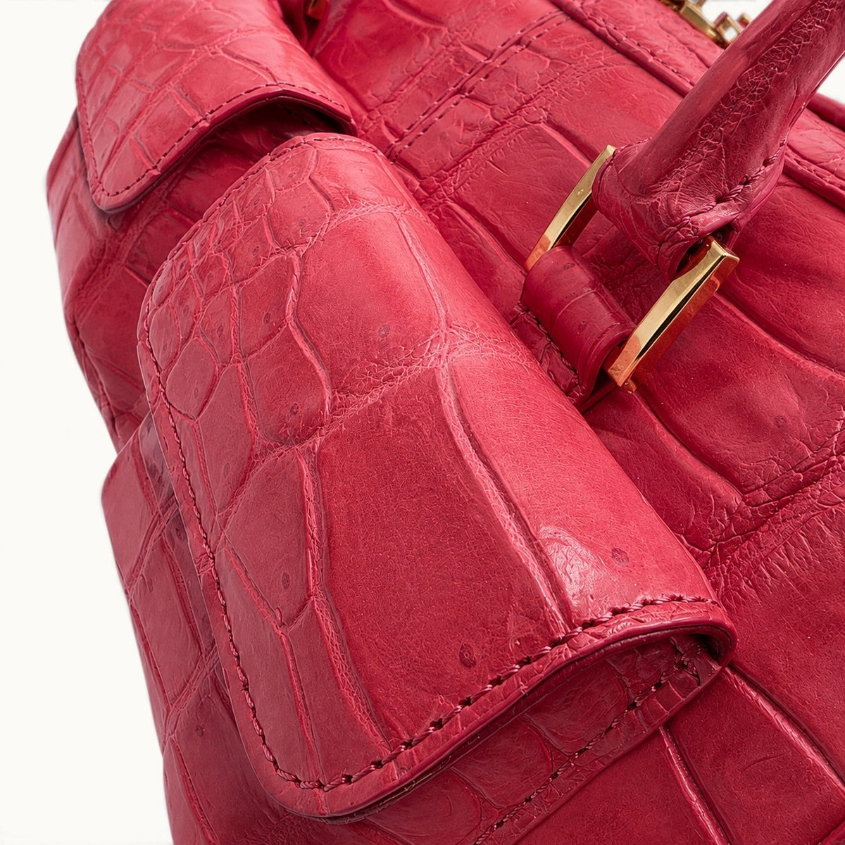 Close-up of coral red crocodile leather highlighting natural scales, fine stitching and polished gold-tone hardware.